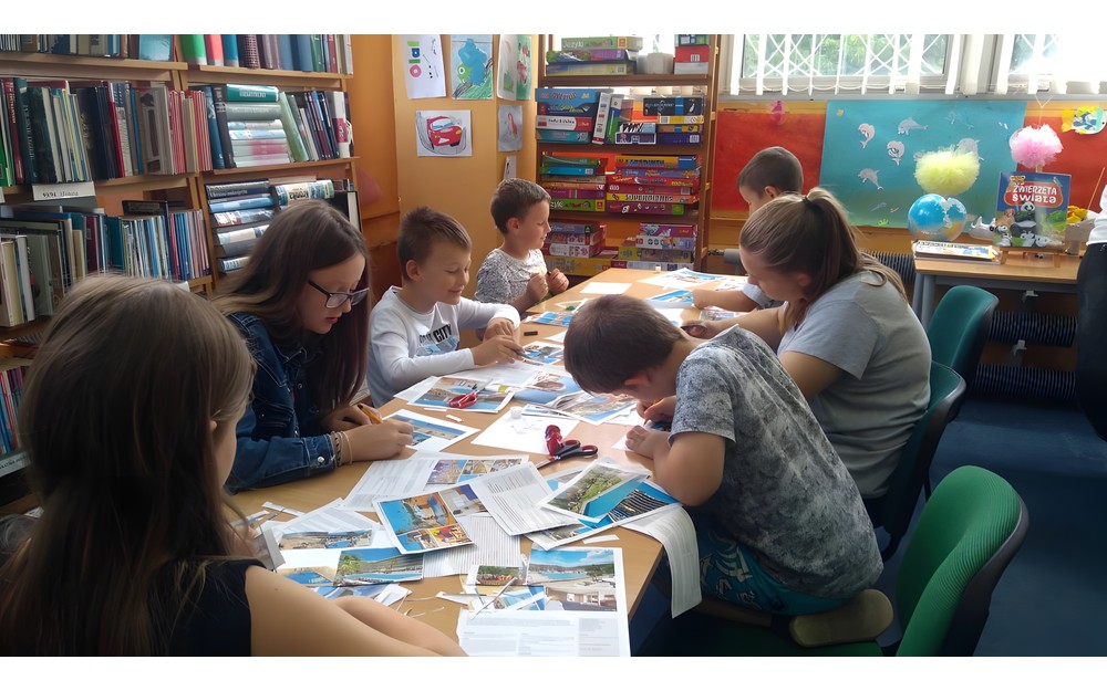 Dzieci siedzą przy stole i wykonują pocztówki