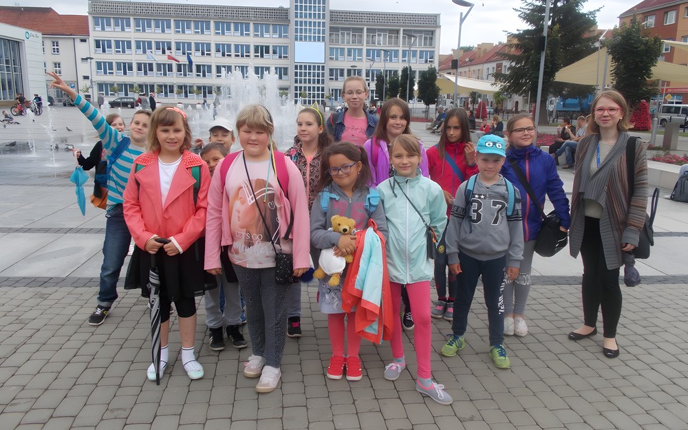 Dzieci wraz z bbliotekarką pozują do zdjęcia przed ratuszem