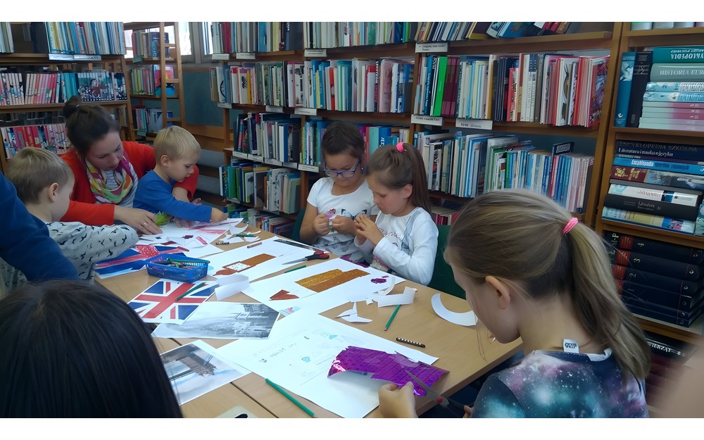 Dzieci siedzą przy stole i wykonują ilustracje zabytków Londynu, a rodzic wspiera ich pracę