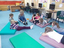 Dzieci siedzą na materacykach słuchając bibliotekarki