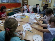 Dzieci siedzą przy stole i wykonują duszki z papierowych talerzyków