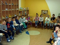 Dzieci siedzą na krzesełkach w półkolu trzymajac pluszowe misie na kolanach