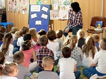 Dzieci siedzą na dywanie i słuchają czytanej przez Panią Wiolę książki 