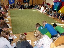 Dzieci zgromadzone wokół dywanu rysują na kartkach portret misia