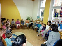 Dzieci siedzą na krzesełkach w kręgu. Bibliotekarka wita się z dziećmi