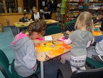 Dzieci siedzą przy stołach i ozdabiają swoje prace