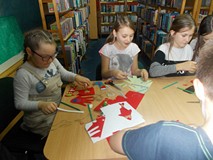 Trzy dziewczynki siedzą przy stole i wykonują świąteczne ozdoby