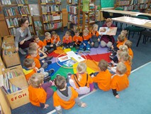 Dzieci siedzą na chuście i słuchają opowiadania czytanego przez bibliotekarkę