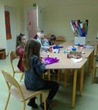 Dzieci przy stołach ozdabiają bombki