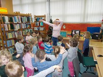 Dzieci stoją przed bibliotekarką tańcząc w rytm muzyki