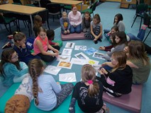 Dzieci siedzą z bibliotekarką na materacach i dopasowują angielskie podpisy do ilustracji związanych