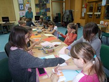 Dzieci siedza przy stołach podczas wykonywania pracy plastycznej