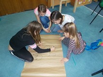 Cztery dziewczynki rysują na szarym papierze konia