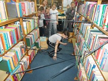 Dziewczynka przechodzi między regałami, pomiędzy którymi jest przymocowana bibuła