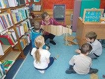 Kilkoro dzieci podziwiają swoją pracę, którą trzyma w rękach bibliotekarka