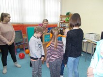 Kilkoro dzieci stoi w grupie, a dziewczynka z zasłoniętymi oczami podaje rękę bibliotekarce