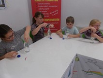 Czworo dzieci wkłada do butelki słomki i spinacze