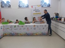 Dzieci siedzą przy stole, a pan tłumaczy co mają zrobić