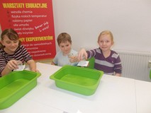 Dzieci trzymają w reku szklanki, prezentując wykonane przez siebie doświadczenia