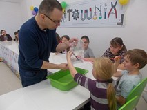 Dzieci wbijają kredkę w worek napełniony wod,  trzymany przez prowadzącego