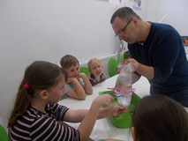 Kilka dziewczynek wbija kredkę w worek trzymany przez prowadzącego warsztaty