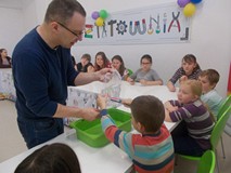 Prowadzący warsztaty trzyma worek z wodą, a dzieci wbijają w niego kredkę