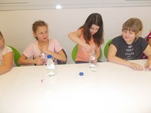 Trzy dziewczynki wkładają do butelki słomki ze spinaczami w ramach eksperymentu