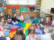 Dzieci siedzą na chuście i słuchają bibliotekarki, która czyta mit