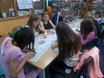 Dzieci wraz z bibliotekarką siedzą przy stole i rzeźbią