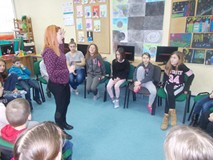 Dzieci siedzą na krzesłach, pośrodku stoi bibliotekarka, która opowiada wymyśloną historię mitologic