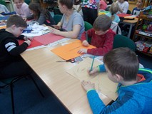 Dzieci siedzą przy stole i rysują cyklopa