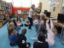 Dzieci siedzą w kręgu, a dziewczynka w środku wybiera dzieci w zabawie