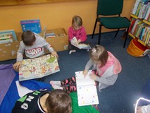 Trójka dzieci siedzi na dywanie i ogląda kiążki