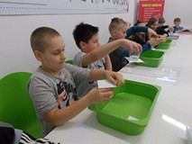 Dzieci siedzą przy stołach i wykonują doświadczenia