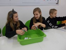 Dzieci siedzą przy stołach i wykonują doświadczenia