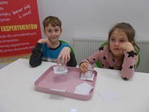 Dziewczynka i chłopiec siedzą przy stole podczas wykonywania doświadczenia z wodą