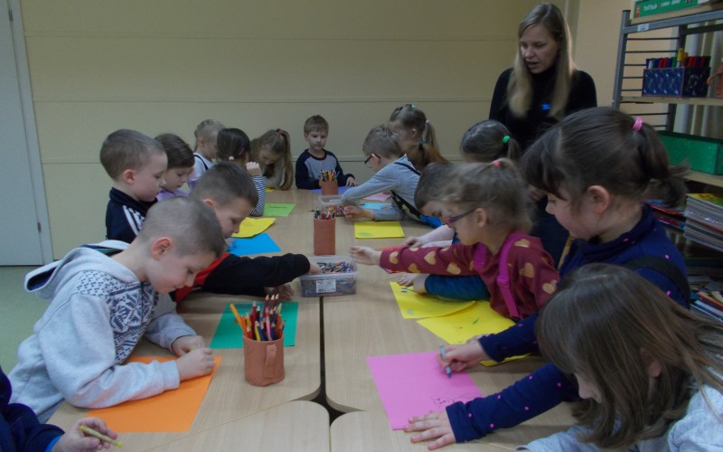 Grupa przedszkolaków przy stołach rysuje ilustracje do opowiadania
