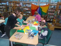 Dzieci siedzą przy stole i wyklejają prace plastyczne na temat sportu