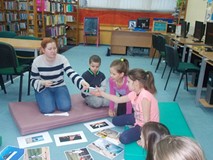 Dzieci wraz z bibliotekarką siedzą na materach, a dzieci dopasowują słownictwo angielskie do kolorow