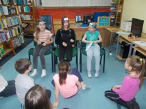 Trzy dziewczynki siedzą na krzesłach z opaskami na głowie i starają się odgadnąć, jakim sportem są