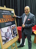 Marek Krajewski po spotkaniu autorskim podpisuje plakat promujący spotkanie