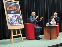 Marek Krajewski w czasie spotkania autorskiego na tle plakatu promującego spotkanie
