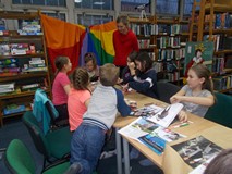 Dzieci siedzą przy stole i pokazują bibliotekarce wykonane prace