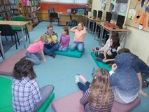 Dzieci siedzą na materacykach i słuchają opowiadania czytanego przez bibliotekarkę