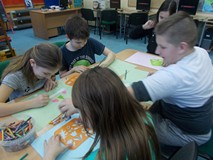 Dzieci siedzą przy stole i wykonuja prace plastyczne