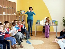 Bibliotekarka pokazuje kształt serca utworzony z palców dłoni, dzieci ją naśladują