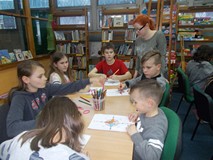 Dzieci kolorują róże wiatru  a bibliotekarka obserwuje ich pracę