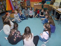 Dzieci wraz z bibliotekarką siedzą w kole i grają w grę