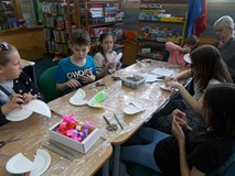 Dzieci wraz z rodzicem siedzą przy stoliku i ozdabiają papugi