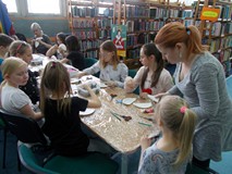 Dzieci wykonują prace plastyczne, a bibliotekarka wspiera ich pracę
